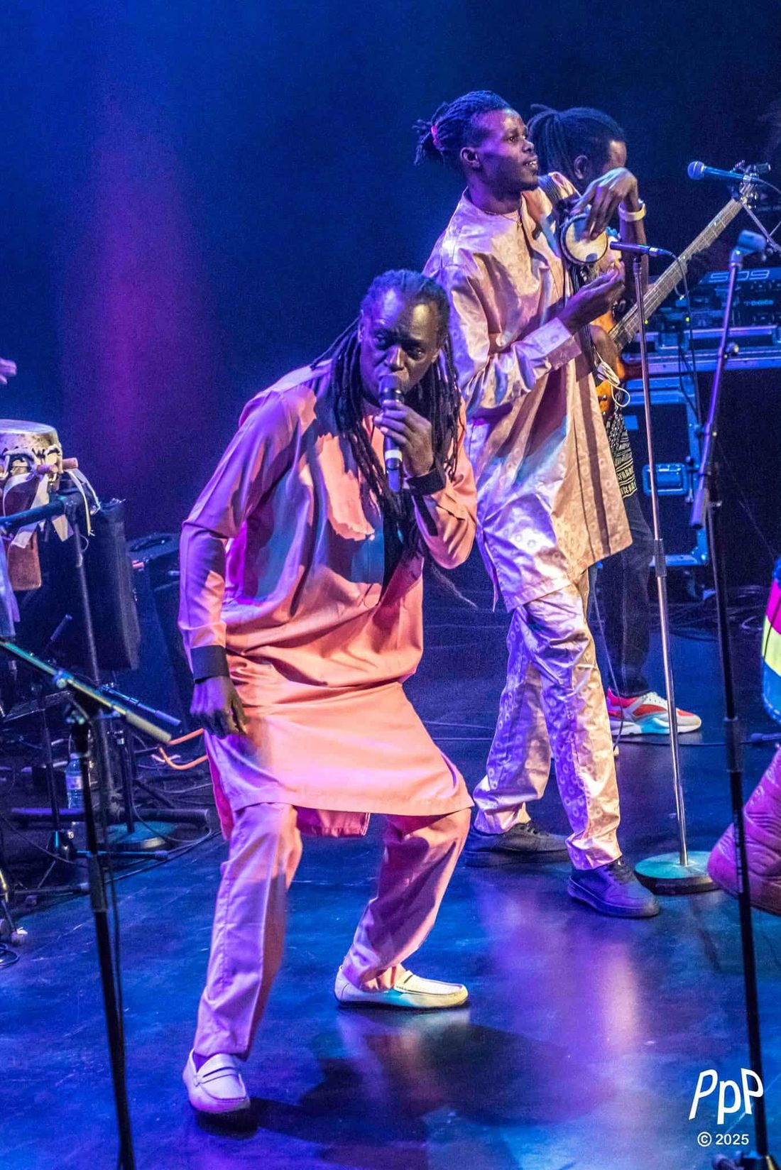 Zale Seck danse, micro en main, un musicien en tenue dorée derrière lui.