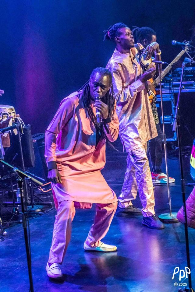 Zale Seck danse, micro en main, un musicien en tenue dorée derrière lui.