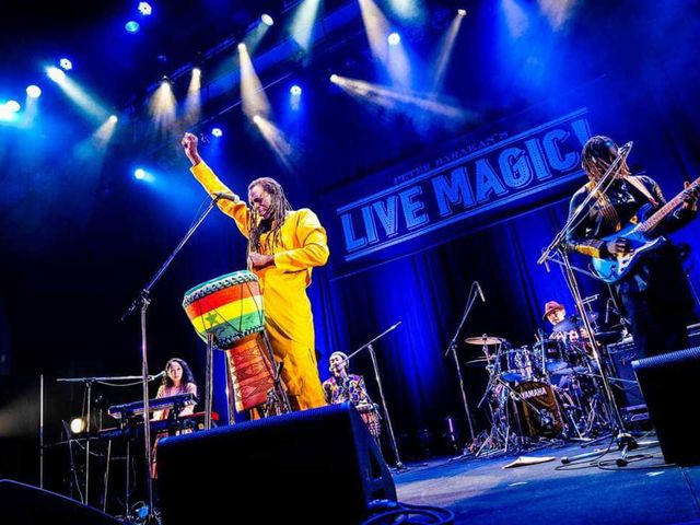 Zale Seck en boubou jaune, bras levé, avec son tama sur une grande scène.