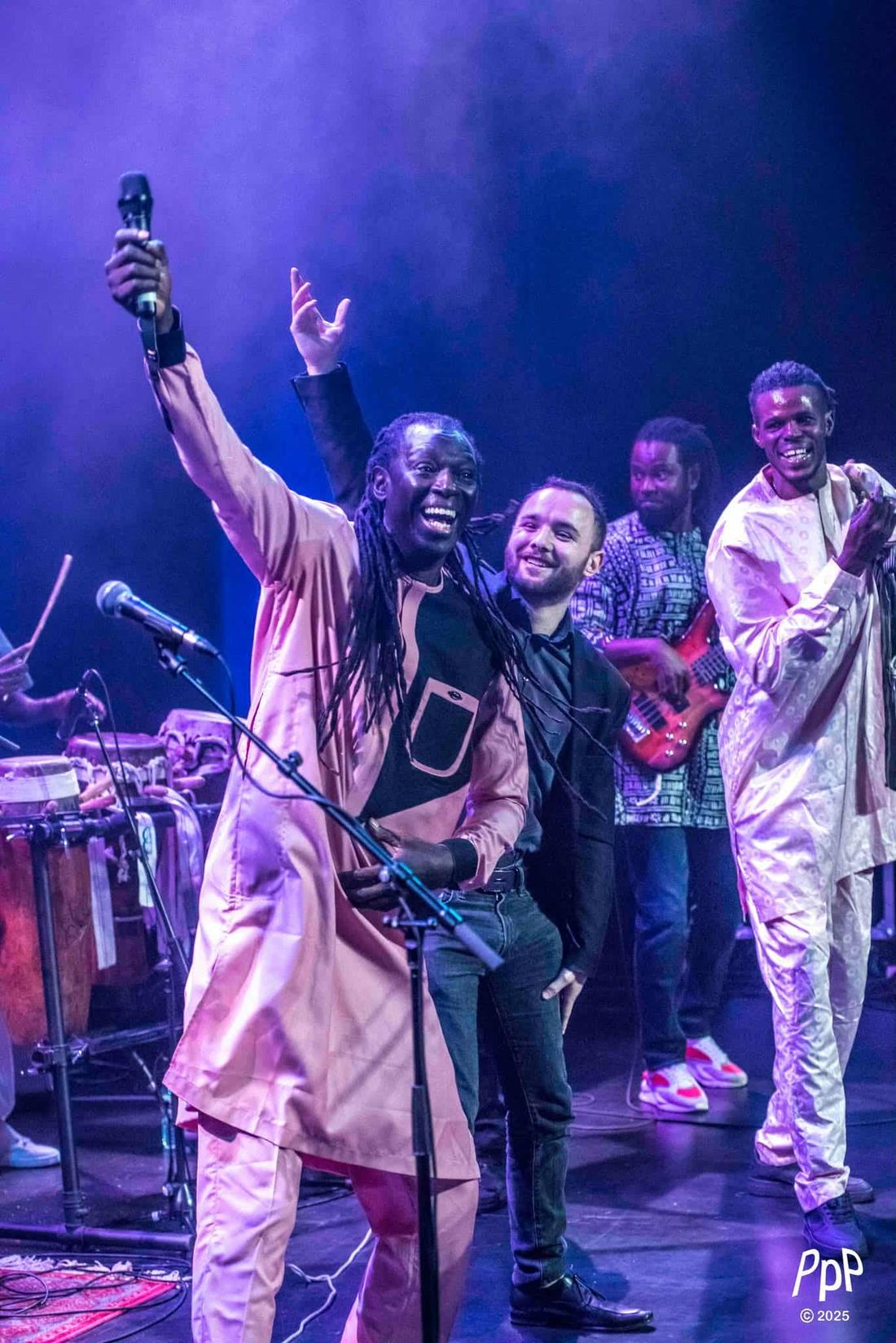 Zale Seck lève le micro, bras ouvert, entouré de ses musiciens sur scène.