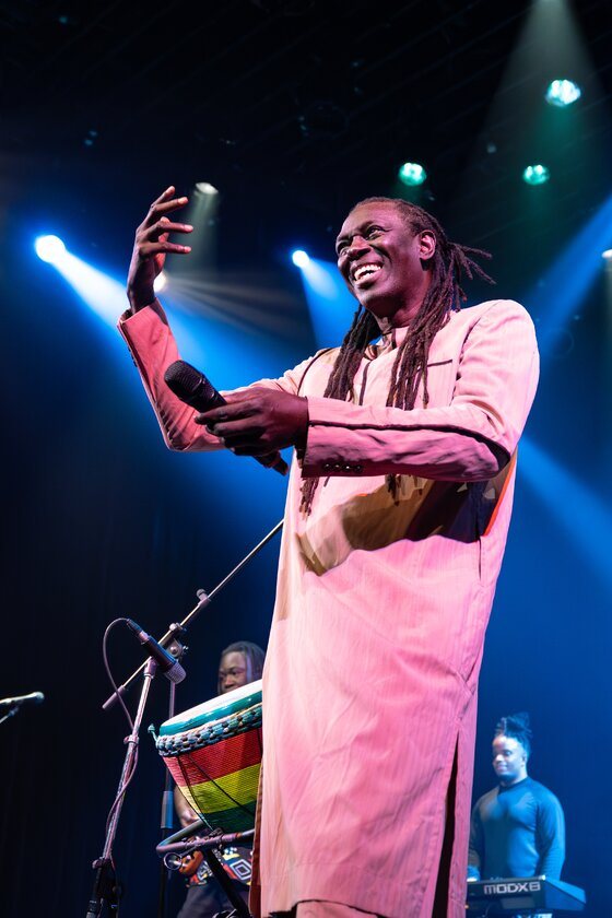 Zale Seck sourit, micro en main, sous les projecteurs bleus.