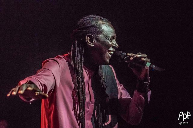 Zale Seck chantant au micro, bras tendu, sur fond noir.