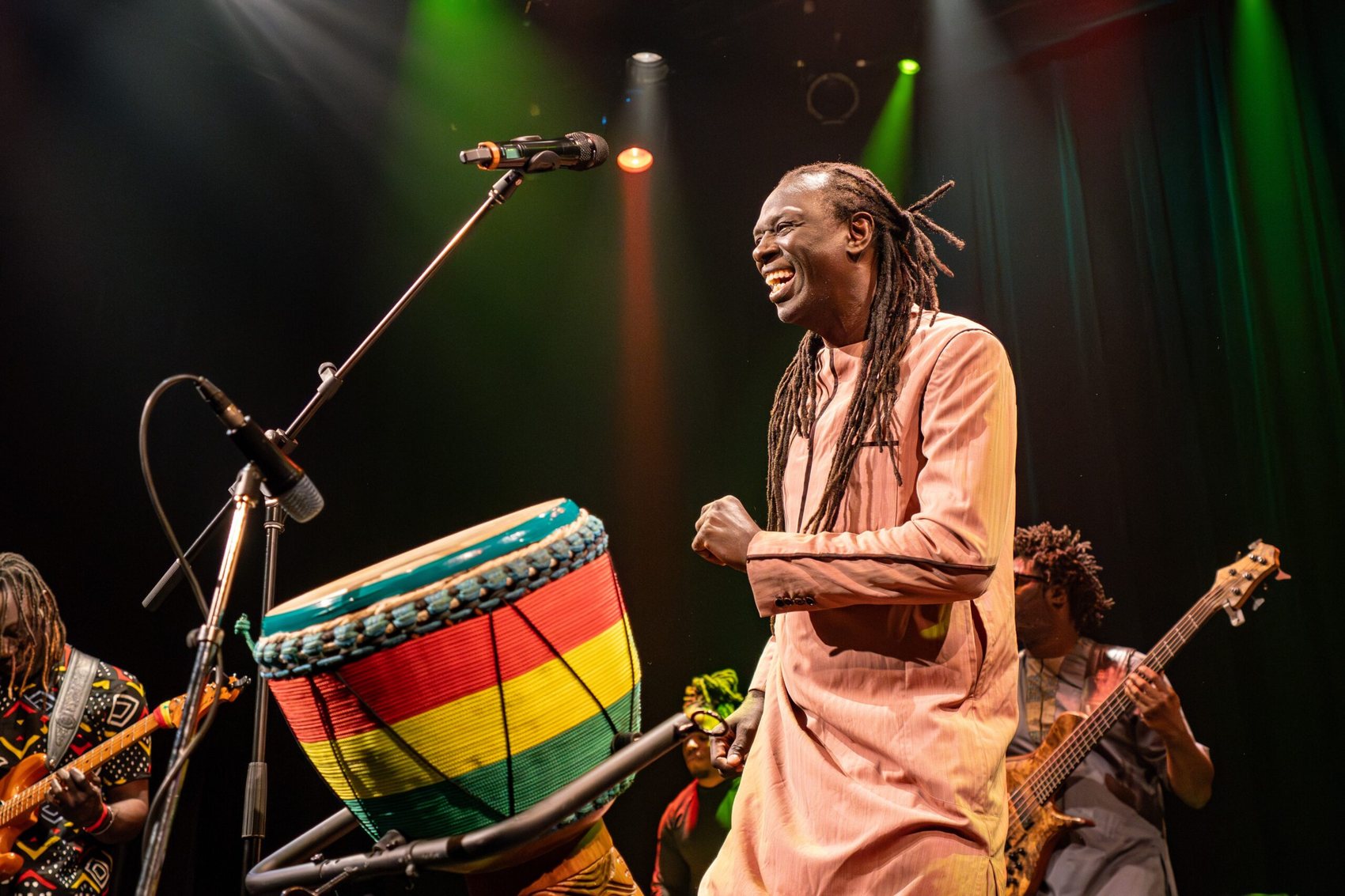 Zale Seck rit sur scène, poing fermé, devant un dundun aux couleurs panafricaines.